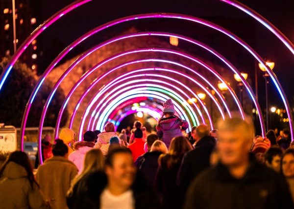 People walking through an illuminated light tunnel made from rings at night time.