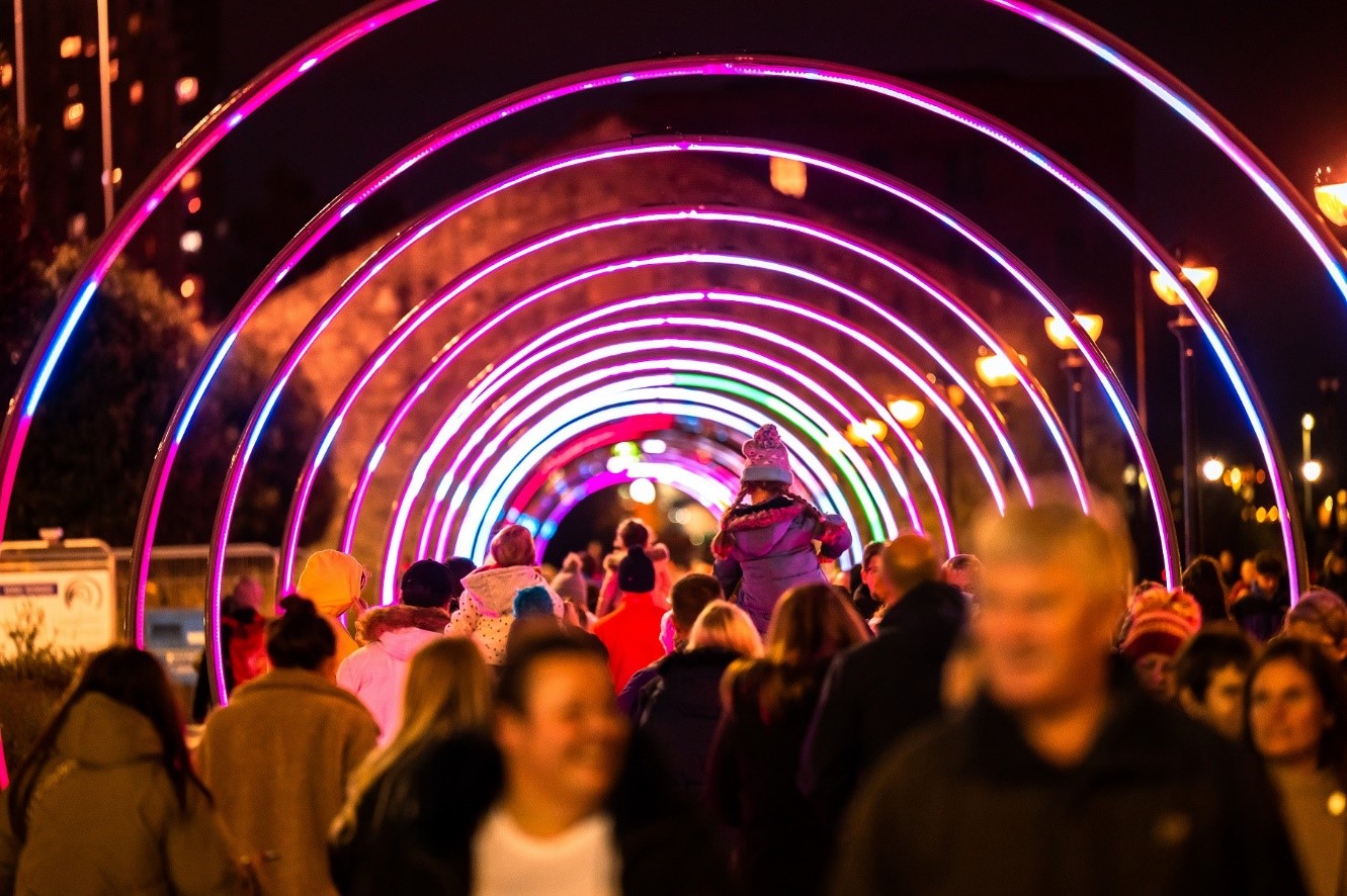 People walking through an illuminated light tunnel made from rings at night time.