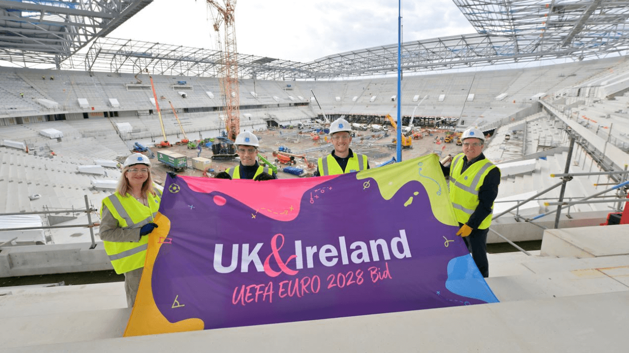 Four people holding a flag that says UK & Ireland inside Everton's Stadium.