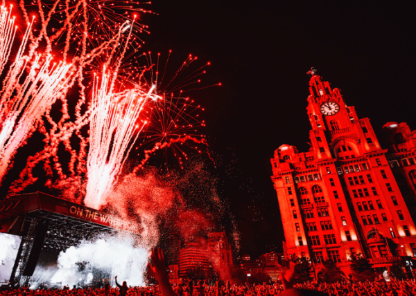 Liverpool pier head with a stage in front of the liver building. Red fireworks are coming from the stage.