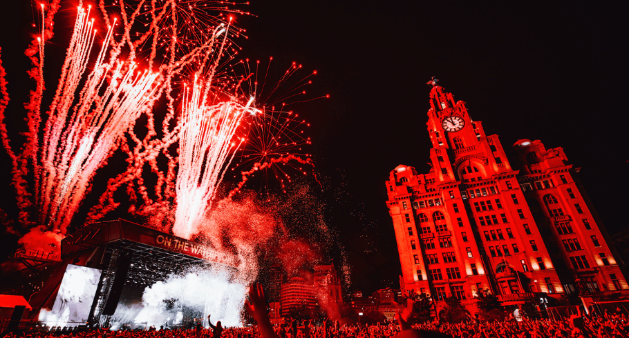 Liverpool pier head with a stage in front of the liver building. Red fireworks are coming from the stage.