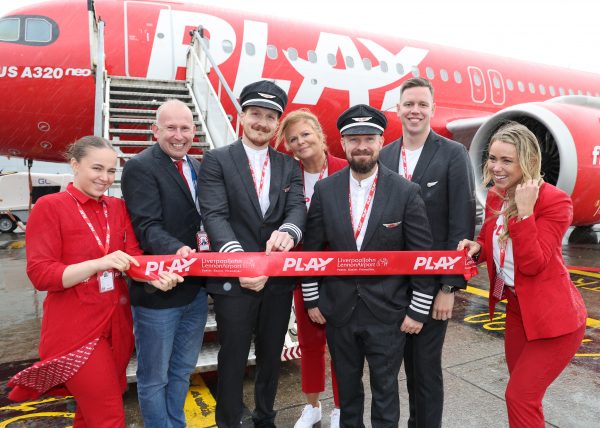 Seven people stood next to a red plane holding up a banner with Play on.