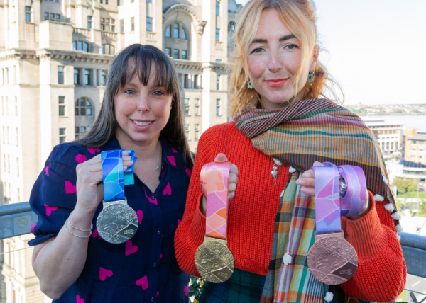 Beth Tweddle and Amy Flynn stood on a rooftop in front of the royal liver building. they are holding three medals that Amy designed for the World Gymnastics Championships Liverpool.
